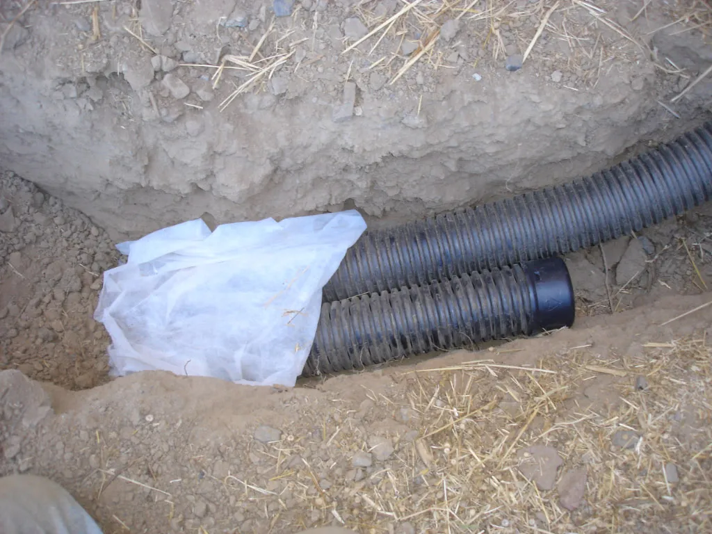 Perforated drainage pipe and filter fabric laid in a trench during a French drain installation